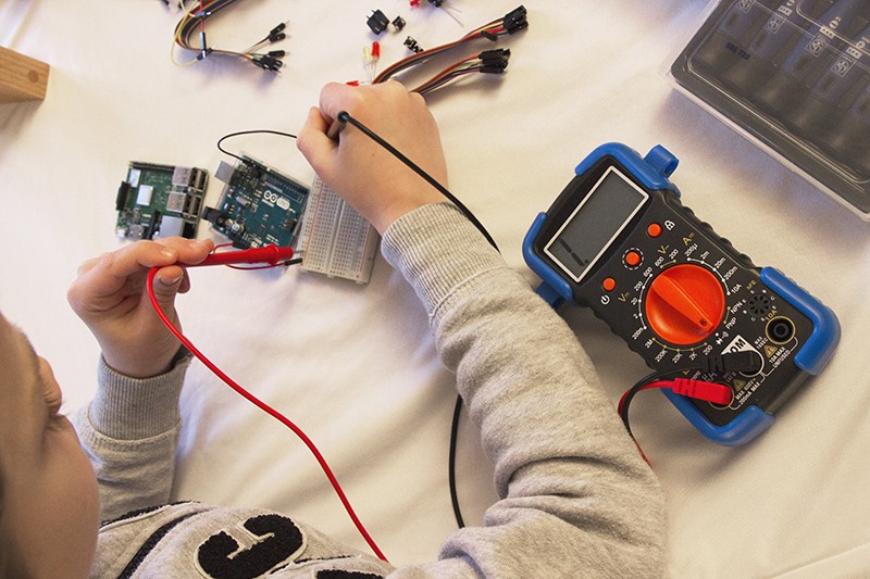 Un enfant utilise un multimètre sur une carte Arduino